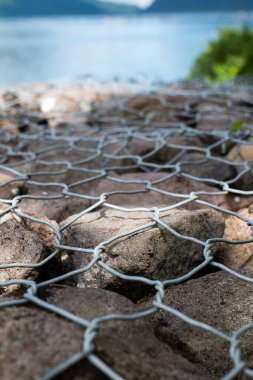Göl kıyısındaki bir taşın üzerindeki metal tel örgüye yakın.