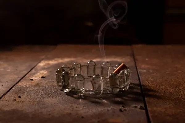one cigarette butt burns in a glass ashtray on a dark background
