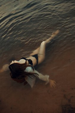 Siyah iç çamaşırlı bir kız ve temiz havada nehirde ıslak beyaz bir gömlek.