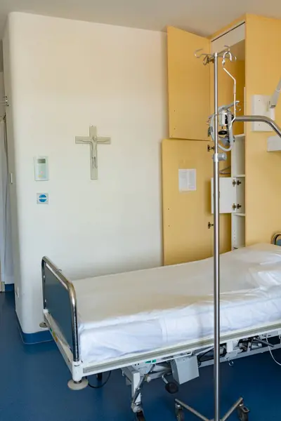 A religious cross is in the spotlight in a hospital ward. Medical equipment with a religious symbol hanging on the wall. An empty hospital room with a drip. Empty hospital bed with intravenous drip in hospital ward.