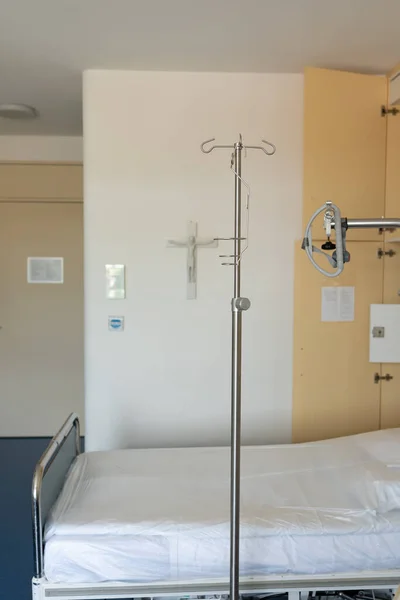Medical equipment with a religious symbol hanging on the wall. An empty hospital room with a drip. Empty hospital bed with intravenous drip in hospital ward.