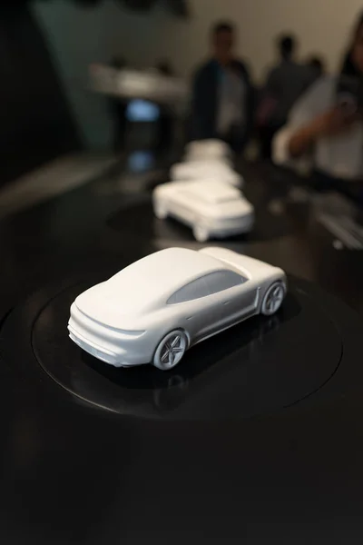 A miniature model of a Porsche car. White car models are displayed as exhibits that people look at. A prototype car. Car model.