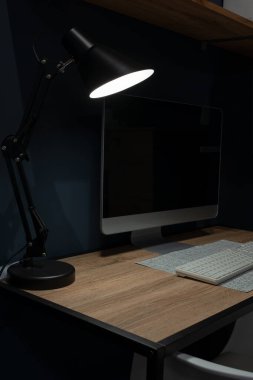 Merkez ofis. Mesai saatlerinde evden çalışma kavramı. Bilgisayar masası karanlık bir odada bir masa lambasıyla aydınlatılır..