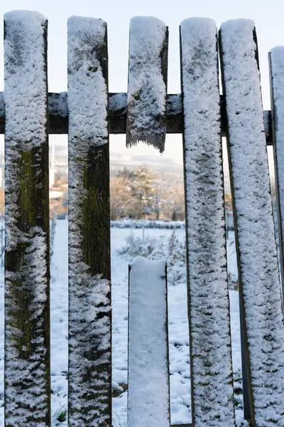 A broken plank on the fence. An ice-covered fence. Wooden fence covered with snow, close-up.