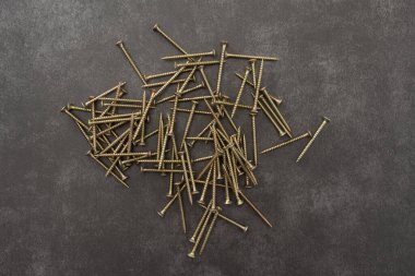 Sarı vidalar gri arka planda. Masaya bir sürü vida saçılmış..