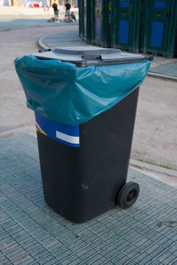 Plastik bir çöp kutusu. Caddenin ortasında büyük siyah bir plastik konteynır duruyor..