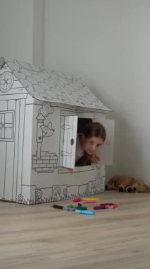 Kız pencereden dışarı bakmaktadır. Çocuklarla oynamak için karton bebek evi. Çocuklar için eğlence ve eğlence.