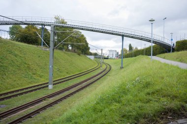 A bending railway in the city. A metal pedestrian bridge passes directly over the railway tracks. clipart