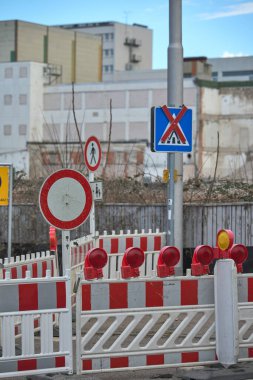 Yol üzerinde bir sürü tabela ve bariyer var. Plastik bariyerler yayaların ve araçların geçişini engelliyor.