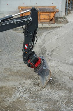 İnşaat alanında Kara Patlama ile Dünya 'yı kazan kazıcı. Kazı kovası iş başında, inşaat alanında toprak topluyor. Siyah patlama makinenin endüstriyel tasarımını vurguluyor.