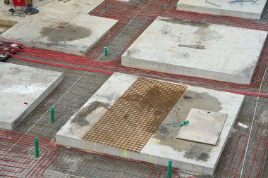 İnşaattaki Plastik Borularla Yeraltı Isıtma Sistemi Kurulumu. Binanın alt kattaki ısıtma sistemi için aralarına kırmızı plastik borular döşenmiş beton temeller..