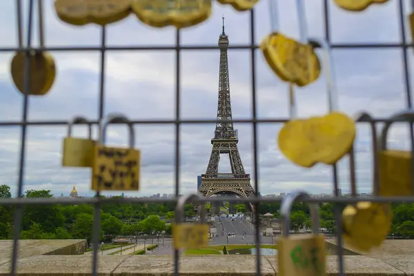 Paris, Fransa 'daki Eyfel Kulesi manzarası. Kapalı sarı kilitler, arka planda Eyfel Kulesi olan uzaktaki bir tel örgüye asılı..