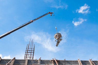 İnşaat alanında mavi gökyüzü arkaplanlı tel üzerinde asılı çimento ya da beton kova