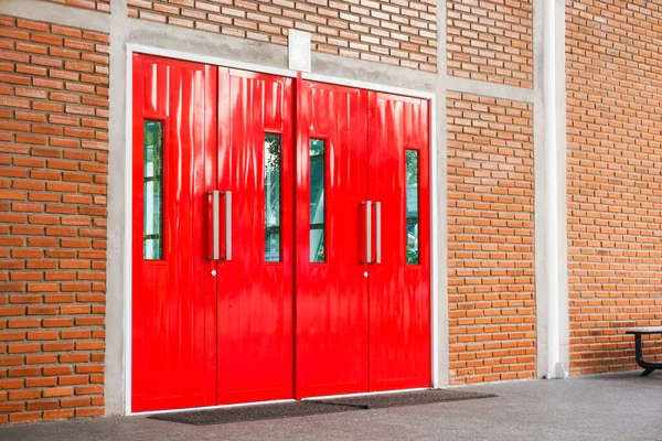 Red modern door with long stainless handle on brick wall at modern building