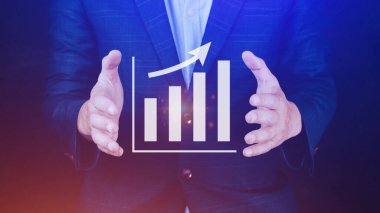 İş adamı grafikte iş büyümesini gösteriyor. Eller grafiklere dokunuyor. Sanal arayüz teknolojisi ve finansal sembollerle artan karı temsil ediyor.