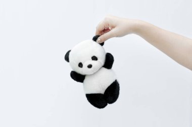 El ele tutuşan panda bebeği, siyah göz kenarları, beyaz arka planda panda oyuncağı.