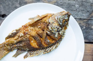 Tahta arka planda beyaz tabak üzerine kızarmış balık Tilapia, Tayland yemeği tarzı.
