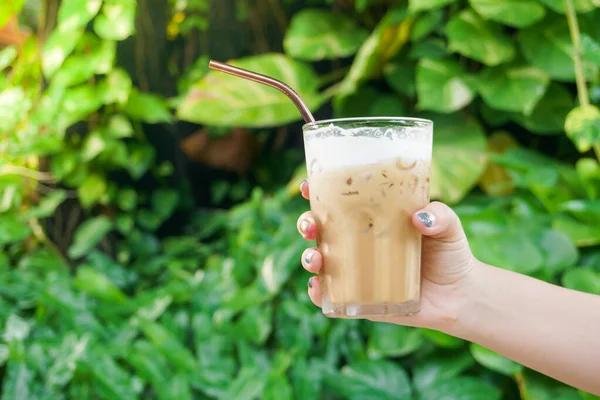 Hand woman holding the glass iced coffee on green nature background,Iced latte coffee