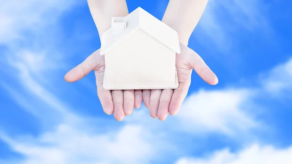 Woman hand holding small home model wooden with cloud blue sky background. Family life and Business real estate concept,Eco house