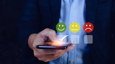İş adamı Smartphone 'da gülen surat ikonunu seçiyor. Geri bildirim derecesi ve olumlu müşteri değerlendirme deneyimi, memnuniyet anketi. ruh sağlığı değerlendirmesi.