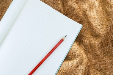 Kahverengi çuval bezinde kalem izolasyonu olan defter, sanat eğitimi için klasik bej kumaş dokusu arka planı.