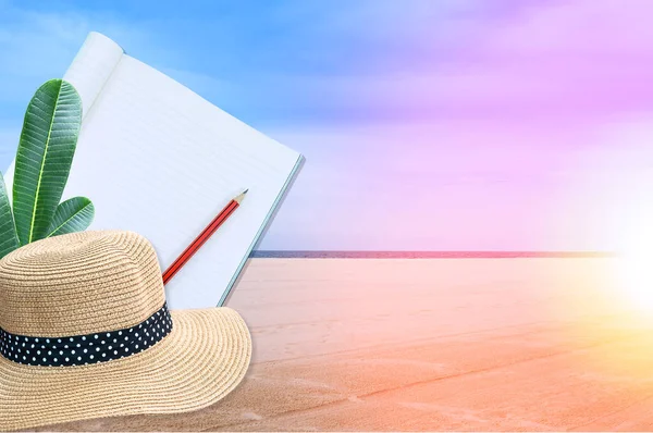 Notebook with pencil and straw hat on sea and sand of a beach nature landscape background