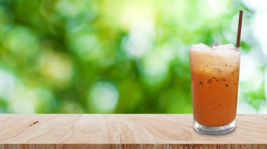 Buzlu Thai sütlü çay, sütlü buzlu çay, Çedar ahşap masada geleneksel Tayland içkisi soyut, bulanık yeşil bokeh arka planı, buzlu yaz içecekleri.