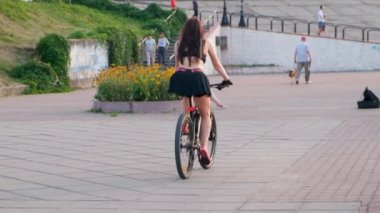Kısa etekli güzel bir atletik seksi kız Obolonskaya seti boyunca bisiklet sürüyor. Kyiv. Ukrayna. İnsanlar yürüyor..