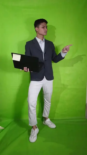 这位英俊的亚洲年轻人拿着一款具有体格特征的移动笔记本电脑 正在展示一些东西 — 图库照片