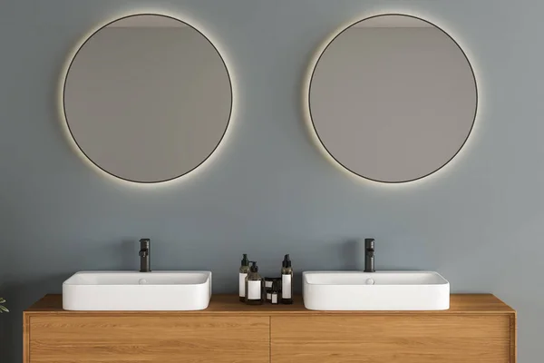 Close up of double sink with oval mirrors standing in on blue wall , wooden cabinet with black faucets in minimalist bathroom. Front view. 3d rendering