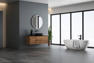 Modern banyo içi mavi ve beyaz tonlu duvar, beton zemin, siyah lavabo ve oval aynalı ahşap kibir, beyaz küvet, panoramik pencereler.