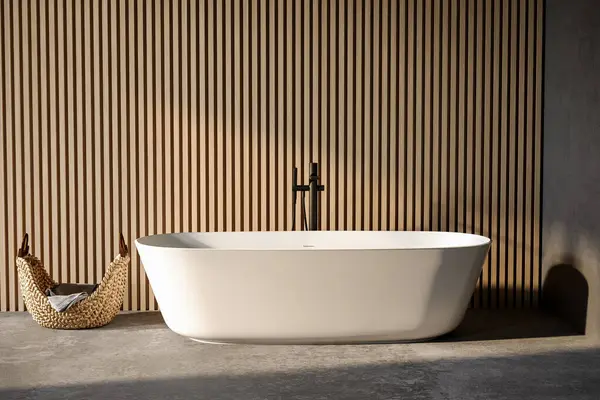 Stylish white bathtub on concrete floor with back faucet in bright bathroom, wooden wall background. Front view.