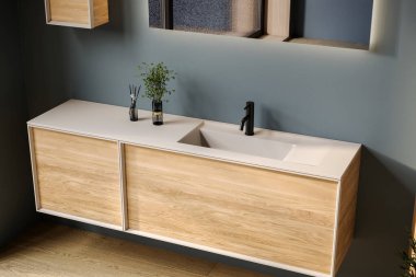 Oval lavabosu olan şık bir banyo, boş tezgah, ahşap kibir, siyah çerçeveli ayna, çiçek ve mavi duvar. Ürünlerinizi şık ve modern bir ortamda sergilemek için ideal..