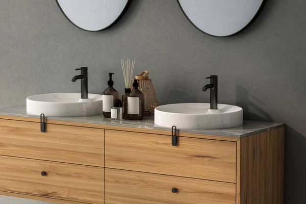 Close up of double sink with oval mirrors- hanging in on dark gray wall, modern cabinet with black faucets in minimalist bathroom