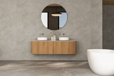 Büyük aynalı ve beyaz küvetli bir banyo. Ayna yuvarlaktır ve üzerinde siyah bir ışık vardır. Banyonun modern ve temiz bir tasarımı var.