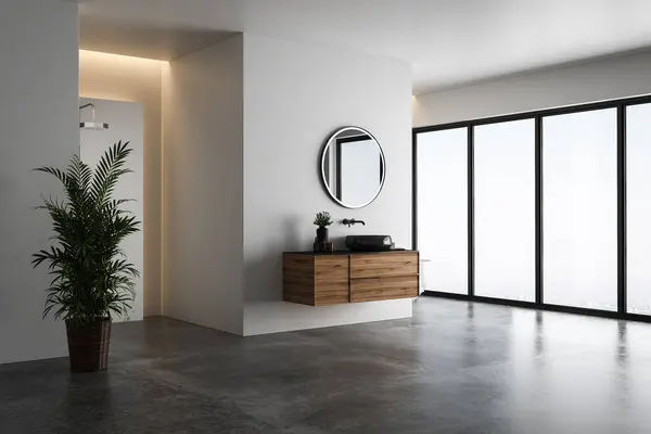 stock image Bright bathroom interior with white tones wall, concrete floor, wooden vanity with black sink and oval mirror, white bathtub, panoramic windows.