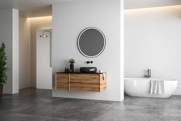 stock image Bright bathroom interior with white tones wall, concrete floor, wooden vanity with black sink and oval mirror, white bathtub, panoramic windows.