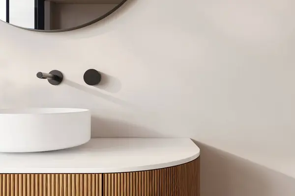 Yuvarlak beyaz bir leğen, dairesel ayna ve minimalist dekorla tamamlanmış flütlü ahşap bir kibrin üzerinde oturur. Bu banyo tasarımı modern zarafet ve doğal dokuların bir karışımını ön plana çıkarıyor..