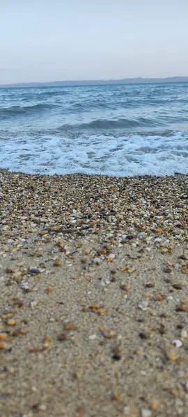 Deniz sahili dikey fotoğrafı. Deniz suyu ve dalgalar. Renkli taşlar ve kumlarla buluşuyor. Harika görüntü..