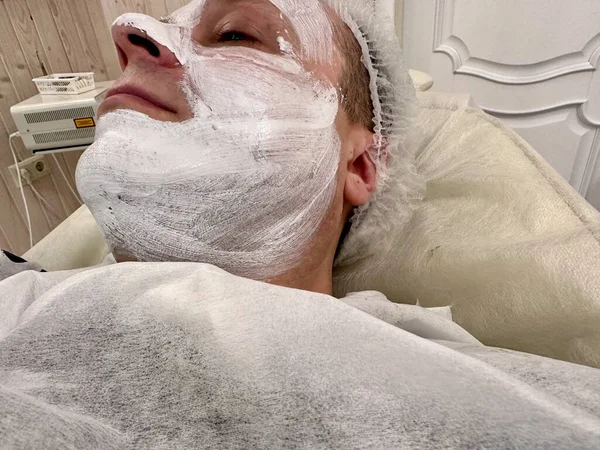 一名年轻人躺在一家化妆品诊所里 眼睛闭着 脸上戴着抗衰老面罩 一个年轻人有一张专业的脸 男子美容院的概念 面部提升的概念 — 图库照片