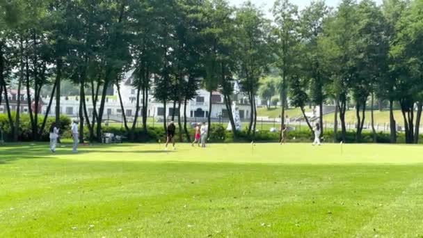 在阳光明媚的夏日 在一个风景秀丽的度假胜地 为旅游姑娘们上关于绿色的高尔夫课 人们在绿树中间的一个球场上打高尔夫 后面是一座漂亮的旅游大楼 — 图库视频影像