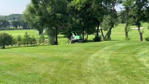 在阳光灿烂的日子里 司机在山坡上驾驶着一台大割草机 在绿色高尔夫球场上割草 修剪草坪 割草的拖拉机 高尔夫球比赛前的草坪护理人员 — 图库视频影像