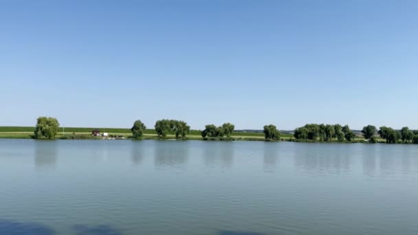 在阳光灿烂的日子里 在蓝蓝的蓝天的背景下 一个美丽的大湖景映衬下 人们带着帐篷在绿树成荫的海岸上休息 在夏天钓鱼 夏天在池塘里休息和钓鱼 — 图库视频影像