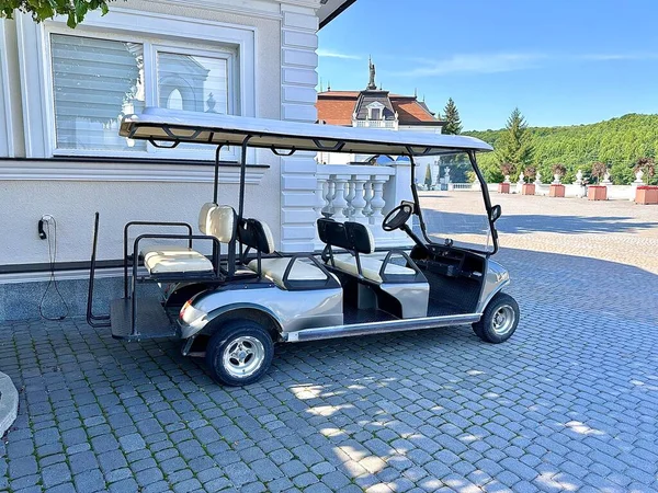 The golf cart is parked at an electric charging station in the yard near the hotel. A golf cart at a luxury resort awaits tourists to take them to the golf course