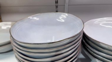 Yemek yemek için çeşitli şekil ve gölgelerden oluşan yeni modern tabaklar bir sofra takımının rafında üst üste dizilmiştir. Raflarda üst üste dizilmiş bir grup seramik tabak. Çanak çömlek, porselen, sofra takımı