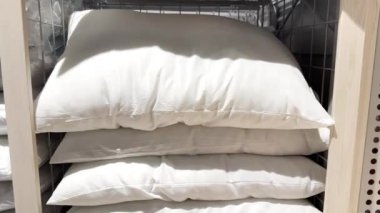 Raflarda üst üste yığılmış beyaz yumuşak yastıklar. Mağazadan yastık seçiyorum. Yatak odası için ürünler.
