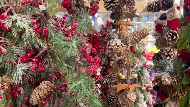 クリスマスマーケットで販売のためのクリスマスの装飾と装飾 お祝いのアクセサリーが店内にあります 家のためのクリスマスの装飾としてコーンが付いている人工常緑の松の枝 — ストック動画