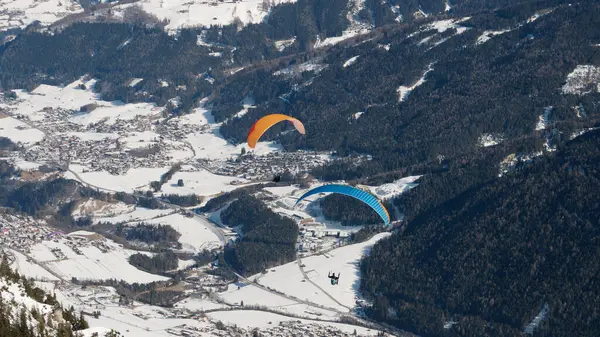Avusturya 'da karla kaplı bir dağın üzerinde uçan paraglider.