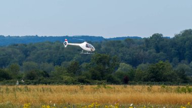 Beyaz bir helikopter yeşil çimlerin üzerinde uçuyor.