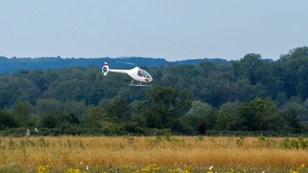 Beyaz bir helikopter yeşil çimlerin üzerinde uçuyor.